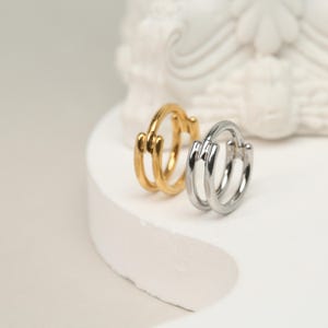 May include: Two hoop earrings, one gold and one silver, with a double-ring design. The earrings are on a white surface.