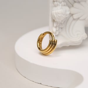 Puede incluir: Aretes de aro dorados con un diseño en capas. Los aretes están hechos de múltiples aros delgados que se apilan uno encima del otro.