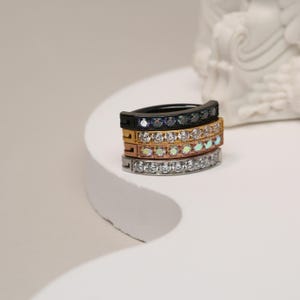 May include: Four hoop earrings with a row of clear cubic zirconia stones. The hoops are stacked on top of each other, with the top hoop being black, the second hoop being gold, the third hoop being rose gold, and the bottom hoop being silver.