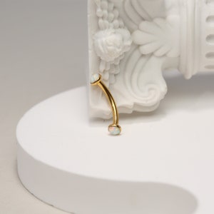 May include: Gold curved barbell with two white opal gems.