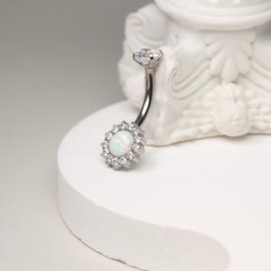 May include: A silver belly button ring with a white opal stone surrounded by clear cubic zirconia stones.