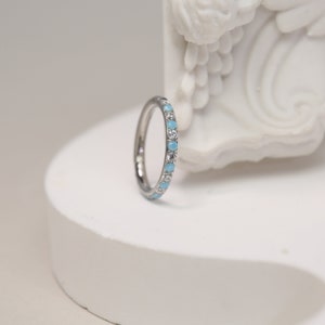 May include: A thin silver band ring with a row of small blue and clear gemstones.