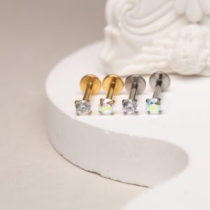 Pode incluir: Três piercings de lábio com gemas transparentes. Os piercings são feitos de aço cirúrgico e vêm em ouro, prata e preto.