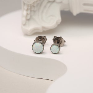 May include: A pair of silver stud earrings with small, round, white opal stones.