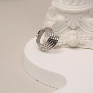 Op de afbeelding: Zilveren creolen met een gelaagd, geometrisch ontwerp. De oorbellen zijn gemaakt van meerdere dunne metalen banden die op elkaar zijn gestapeld.