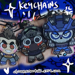 Puede incluir: Tres llaveros de personajes de dibujos animados con anillas negras. Los llaveros presentan personajes en azul, gris y marrón con el texto "keychains" y "clownsmoothie.etsy.com" en blanco.