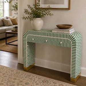 May include: A rectangular console table featuring a green and white striped pattern across its surface. The table has three small round knobs on the front drawer and is supported by two legs with gold-toned metal bases at the bottom of each side.