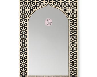 May include: A rectangular wall mirror featuring an arched top and a frame decorated with a repeating black and cream floral geometric pattern. The glass surface displays a circular logo with the letters UR in the center of the reflective area.
