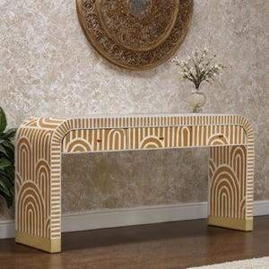 May include: A white and gold console table with a curved design. The table features a repeating pattern of arches and stripes. It has two drawers with gold hardware and gold accents on the base.