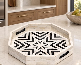 May include: An octagonal serving tray featuring a geometric star pattern in black and white. The tray is constructed from small, rectangular pieces of off-white material with a smooth finish and includes two black cutout handles on opposite sides.