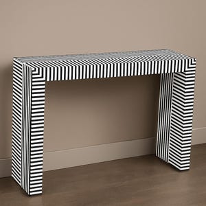 May include: A modern console table with a striking black and white striped pattern. The table has a rectangular top and two supporting legs, creating a minimalist design. The dimensions are approximately 48 inches long, 16 inches wide, and 30 inches high.