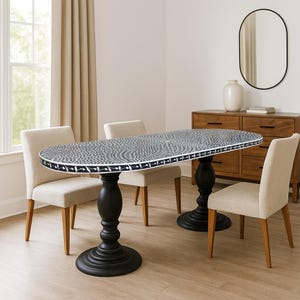 May include: An oval dining table with a patterned top and black pedestal base. The table is surrounded by four beige upholstered chairs. A wooden cabinet, mirror, and vase are in the background, creating a dining room setting.