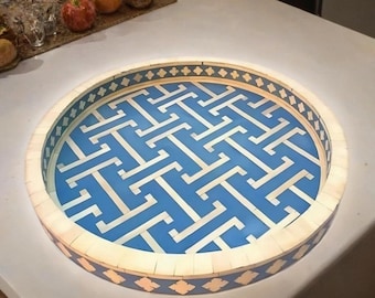 May include: A round decorative tray with a blue and white geometric pattern. The tray has a cream-colored border with a repeating diamond design. The tray is made of wood and is suitable for serving or display.