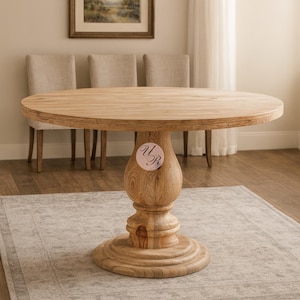 May include: A round wooden dining table with a pedestal base. The table is made of light-colored wood and has a natural finish. The pedestal base is intricately carved. The table is surrounded by three beige upholstered chairs.