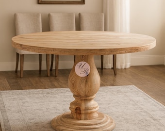 May include: A round wooden dining table with a pedestal base. The table is made of light-colored wood and has a natural finish. The pedestal base is intricately carved. The table is surrounded by three beige upholstered chairs.