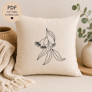 May include: Square cream cushion featuring a black embroidered botanical design. The design depicts a stylized eucalyptus branch with leaves, flowers, and buds. The cushion has the text "PDF PATTERN DOWNLOAD" in a circle.