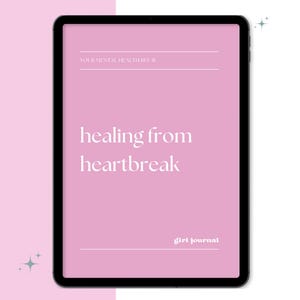 May include: A digital tablet displays a pink screen with the words "healing from heartbreak" in a white, elegant font. The text "YOUR MENTAL HEALTH BFE" and "girl journal" are also visible. The tablet has a black border and is set against a white background.