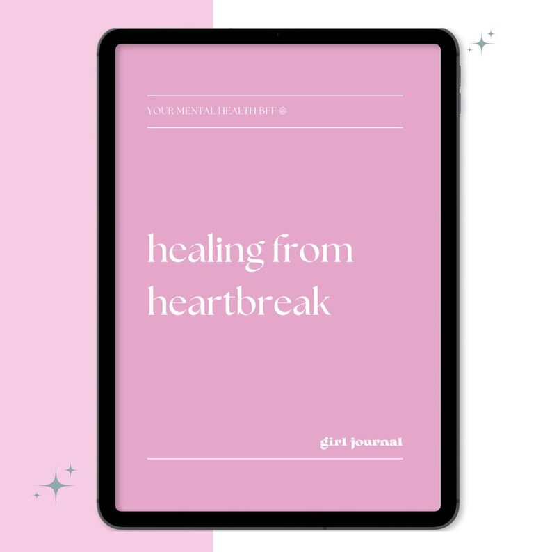 May include: A digital tablet displays a pink screen with the words "healing from heartbreak" in a white, elegant font. The text "YOUR MENTAL HEALTH BFE" and "girl journal" are also visible. The tablet has a black border and is set against a white background.