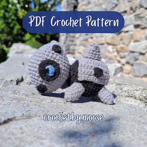 May include: Crocheted gray and black amigurumi toy with blue eyes. The toy is sitting on a gray stone surface. The text "PDF Crochet Pattern" and "crochet.by.moose" are visible in the image.