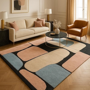May include: A modern area rug with an abstract design. The rug features large, irregular shapes in shades of peach, beige, and blue against a black background. The rug is placed in a living room with a sofa, armchair, and coffee table.