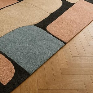 May include: A modern area rug with a geometric design. The rug features large, irregular shapes in shades of beige, peach, and blue, separated by black lines. The rug is placed on a wooden floor with a herringbone pattern.