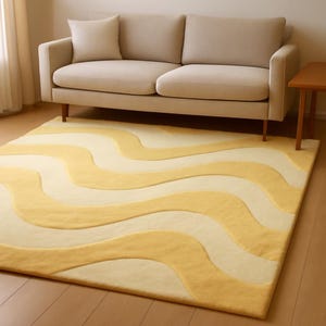 Hand‑tufted wool rug with soft butter yellow and cream wavy pattern, low pile, rectangular, styled under a beige sofa in a bright living room.
