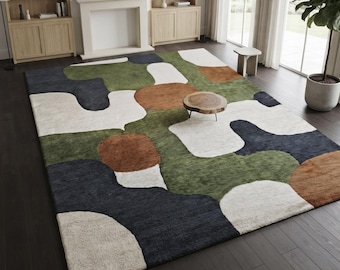 May include: A large rectangular area rug featuring an abstract pattern of organic, rounded shapes in shades of olive green, charcoal gray, cream, and burnt orange. The rug has a textured pile surface and covers a dark wood floor.