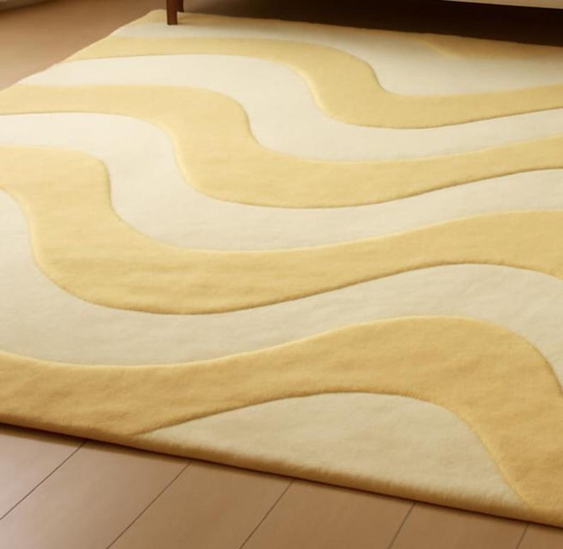 A hand-tufted wool rug on a wooden floor featuring an abstract wavy pattern in alternating bands of butter yellow and cream.