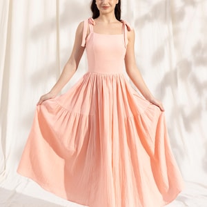 May include: A peach-colored tiered maxi dress with thin straps that tie at the shoulders. The dress has a square neckline and a flowy skirt.