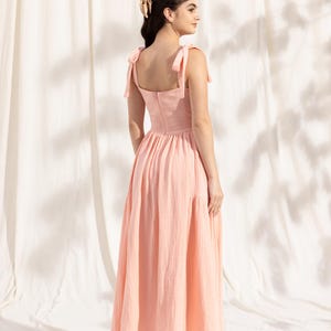 May include: A light pink midi dress with a square neckline and thin straps that tie at the shoulders. The dress has a gathered skirt and a back zipper closure.