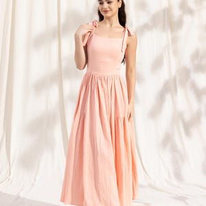 May include: A peach-colored tiered maxi dress with thin straps that tie at the shoulders. The dress has a square neckline and a flowy, A-line silhouette.
