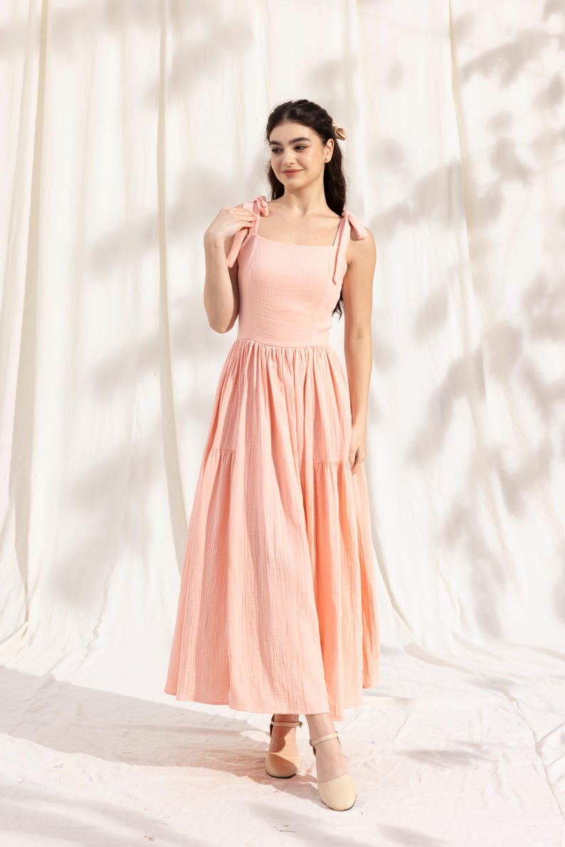May include: A peach-colored tiered maxi dress with thin straps that tie at the shoulders. The dress has a square neckline and a flowy, A-line silhouette.