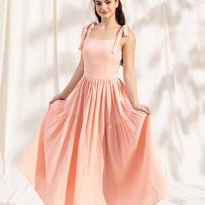 May include: A light pink tiered maxi dress with thin straps that tie at the shoulders. The dress has a square neckline and a flowy skirt.