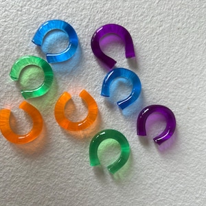 Könnte beinhalten: Ein Satz von neun bunten Kunststoffringen, die jeweils die Form eines Hufeisens haben. Die Ringe sind in Blautönen, Grün, Orange und Lila.