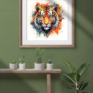 Op de afbeelding: Een ingelijst aquarel schilderij van een tijgerkop met oranje, gele en blauwe verfspatten. Het schilderij hangt aan een groene muur met een houten plank eronder. De plank heeft vier kleine potplanten met cactussen en een grotere potplant met groene bladeren.