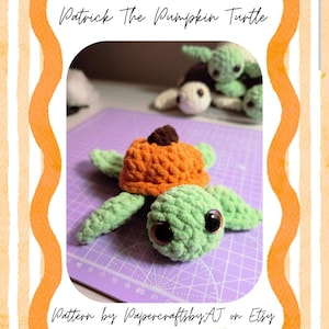 May include: A crochet turtle toy with a light green body and a textured orange pumpkin shell featuring a small brown stem. The turtle has large dark eyes and is positioned on a purple cutting mat. The text reads Patrick The Pumpkin Turtle.