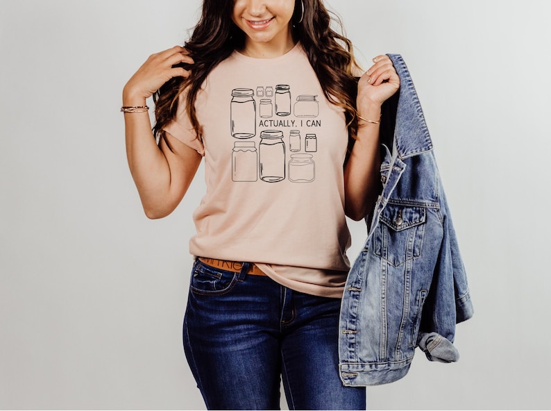 May include: A light pink t-shirt with a graphic of multiple mason jars and the text "Actually, I can".
