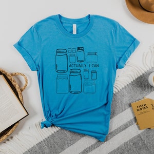 May include: A turquoise blue t-shirt with a graphic of jars and the text "Actually, I can".