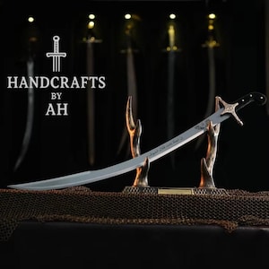 May include: A curved sword with a silver blade and a black handle, presented on a decorative stand. The stand is bronze-coloured and has a chainmail base. The image includes the text "HANDCRAFTS BY AH".