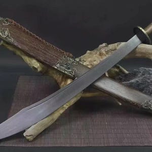 May include: A traditional Chinese sword with a curved blade, resting in its wooden scabbard. The hilt and scabbard feature ornate metal detailing. The sword is displayed on a wooden surface, showcasing its craftsmanship.
