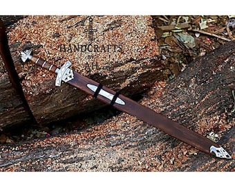 May include: A handcrafted sword with a dark wooden scabbard and handle, featuring silver-colored metal accents. The sword rests on a textured, brown wooden surface. The text "HANDCRAFTS ATLH" is visible.