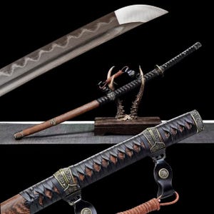 May include: A Japanese katana sword with a curved blade and a wooden handle. The sword features a black handle wrap and decorative metal accents. The blade has a silver finish with a visible pattern. The sword is displayed on a wooden stand.