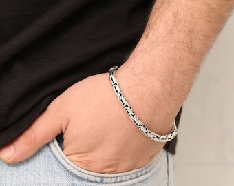 May include: A silver chain bracelet with a box chain design. The bracelet is on a person's wrist.