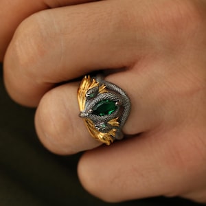 May include: A silver and gold ring with a snake motif. The ring features a pear-shaped, emerald-green gemstone. The snake's body is silver, and the accents are gold.