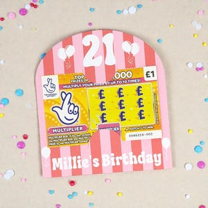 May include: A pink and white birthday card with a scratch-off lottery ticket. The card features the number 21, balloons, and the text "Millie's Birthday." The lottery ticket shows the National Lottery logo and the text "MULTIPLIER."