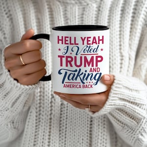 May include: White ceramic coffee mug with a black rim and handle. The mug has a red and blue design with the text "Hell Yeah *I Voted* Trump and Taking America Back".
