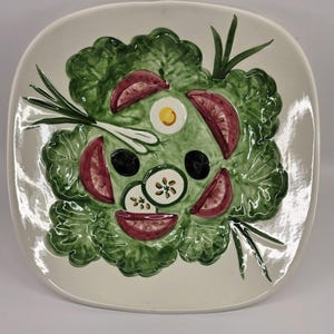 May include: A white ceramic salad plate with a green lettuce design and red tomato slices, cucumber slices, and a fried egg.