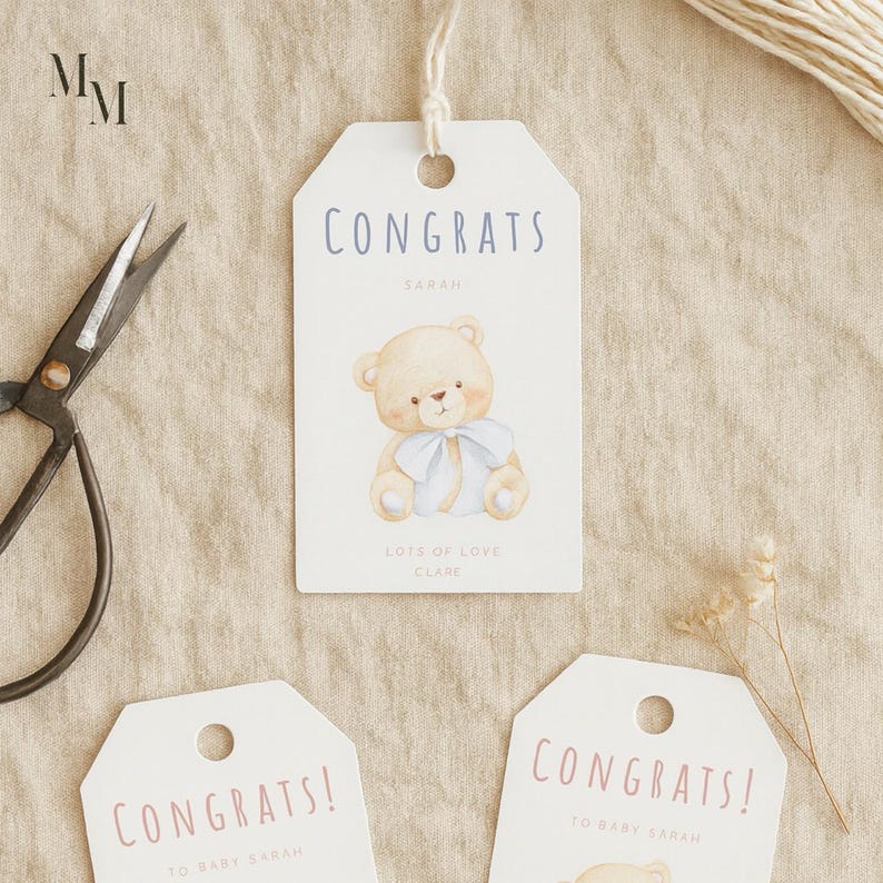 May include: White gift tags with the word "CONGRATS" in blue or pink lettering. One tag features a teddy bear illustration with a blue bow. The tags are tied with twine and are suitable for baby showers or new baby gifts.