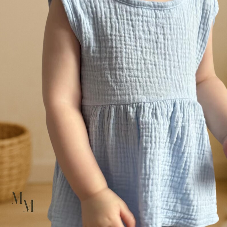 May include: A light blue, sleeveless baby dress with a textured, crinkled fabric. The dress has a round neckline and a gathered waist, creating a flowing silhouette. The dress is made of a soft, lightweight material.
