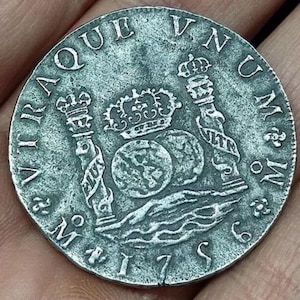 May include: A detailed silver coin with text and decorative elements. The coin showcases a central design with crowns and spheres, encircled by inscriptions and the date 1769. The coin has a weathered, antique look.